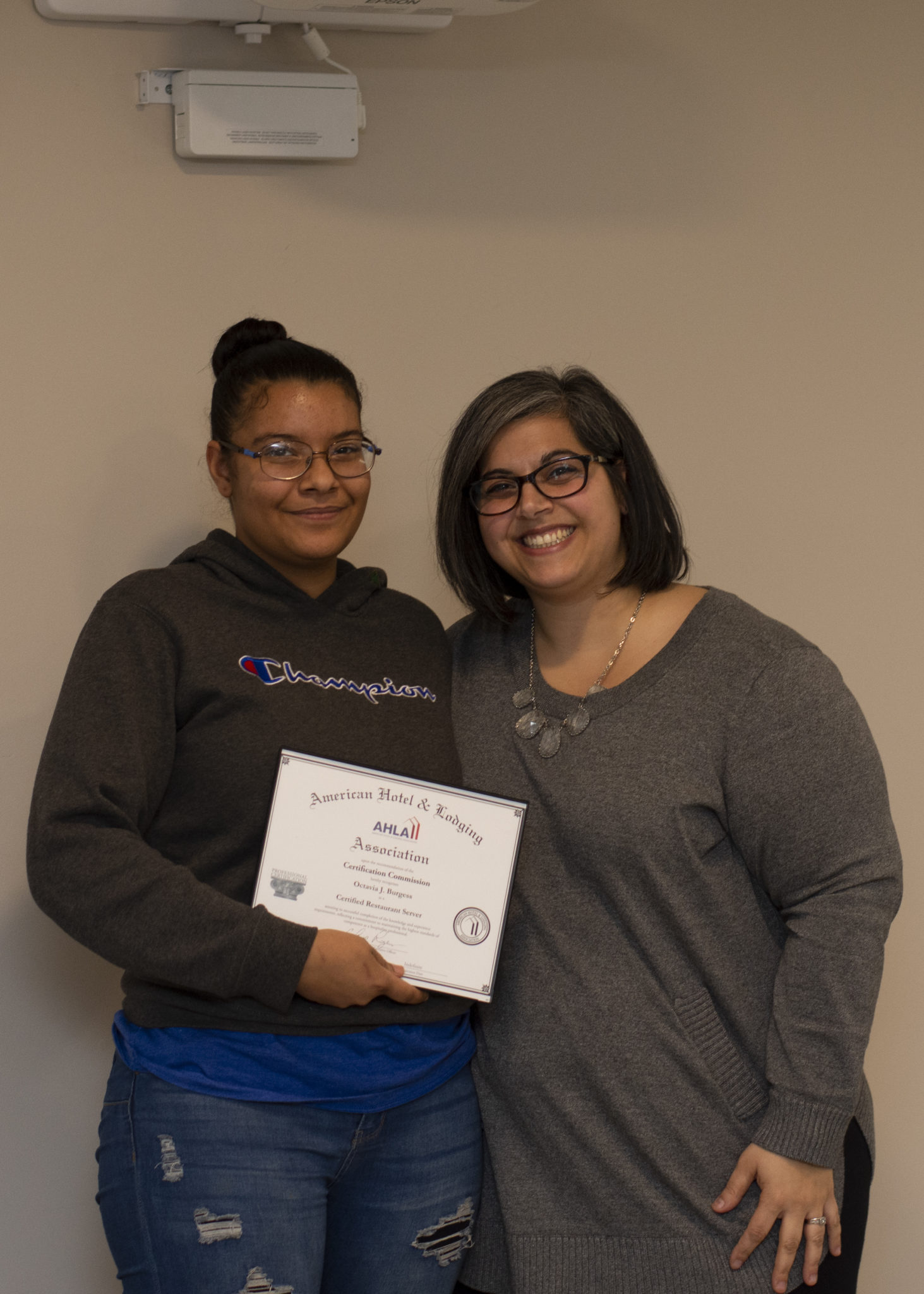 Two women smile at the camera, with one holding a certificate