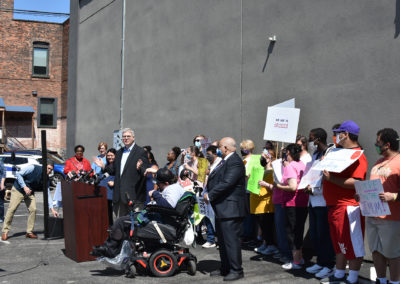 A man speaks at a podium with a group of supporters behind him