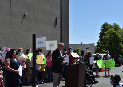 A man speaks at a podium with a group of supporters behind him